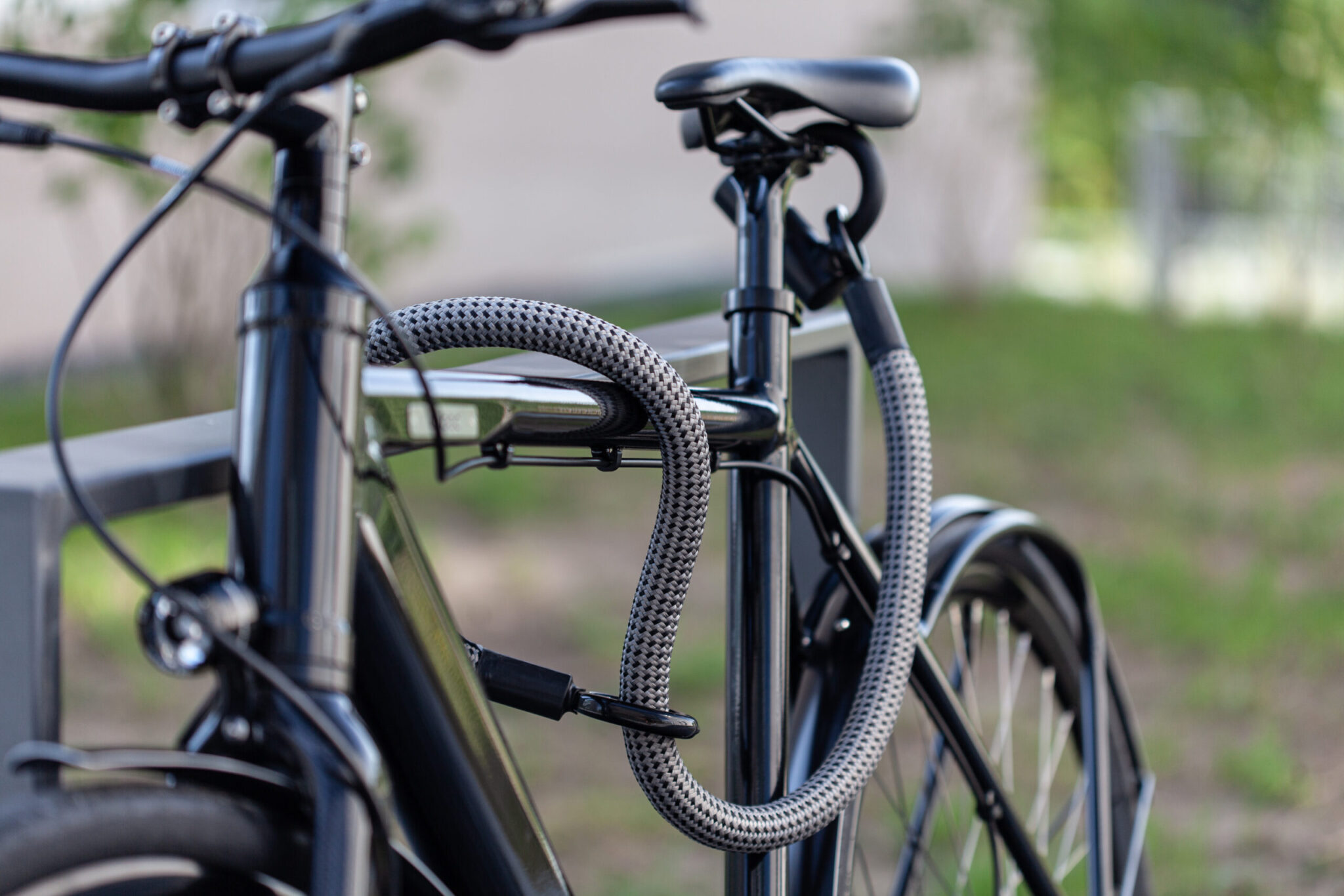 Flexible U-lock extension tex-lock eyelet in gray encloses bike frame on bike stand