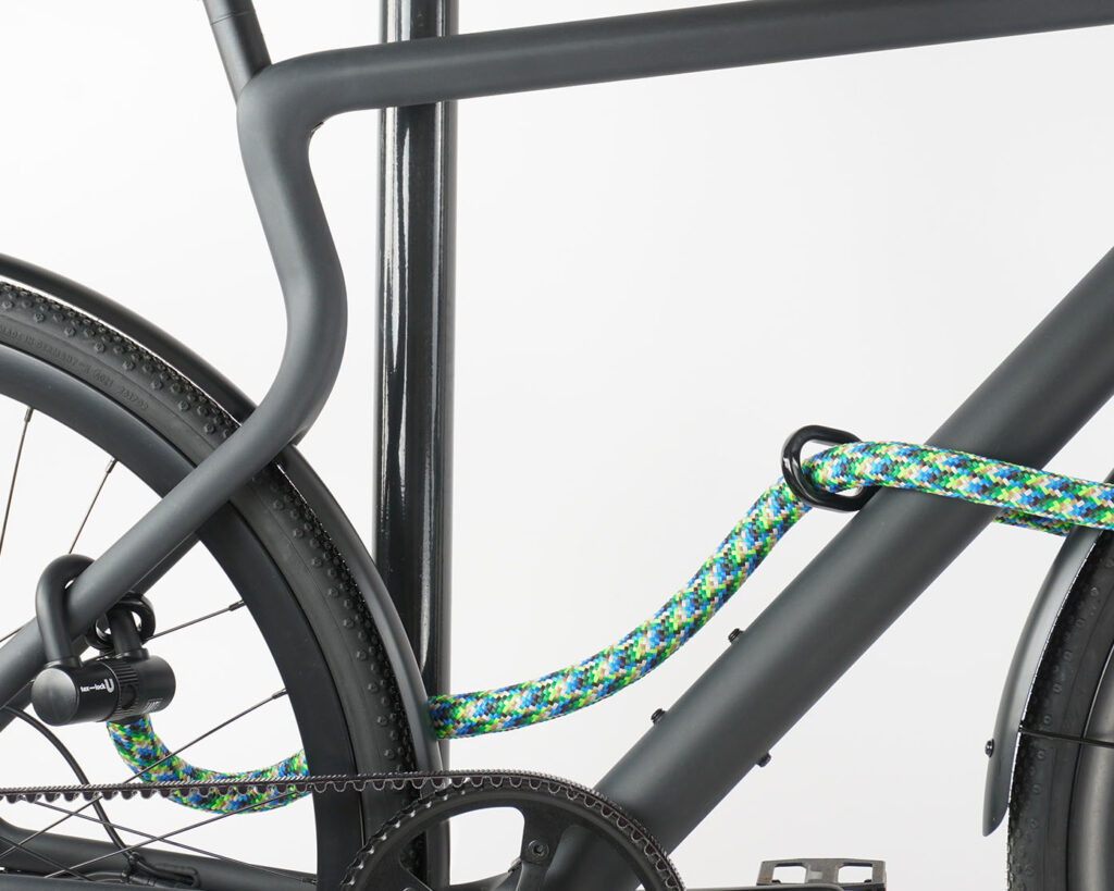 Kleines Bügelschloss mit Verlängerung aus buntem Textil sichert Vorder- und Hinterrad gleichzeitig am Fahrradständer ab
