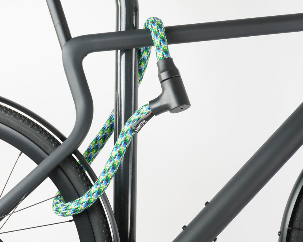 Hinterrad und Oberrohr vom Fahrrad mit buntem Seilschloss aus Textil an Fahrradständer angeschlossen