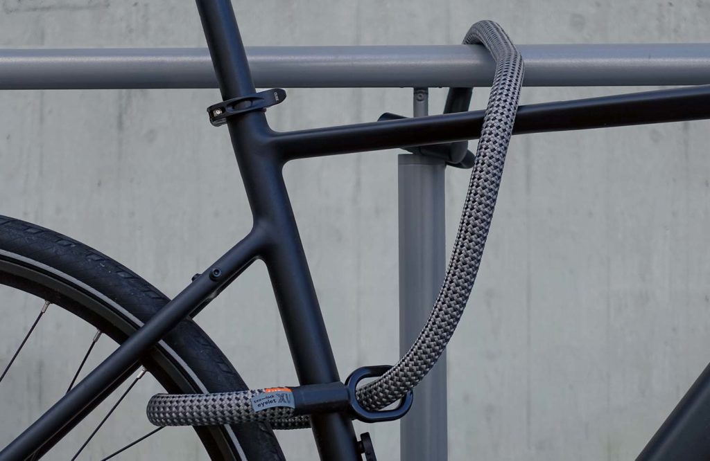 Fahrrad am Rahmen und Hinterrad mit Fahrradschloss aus Textil an Fahrradständer angeschlossen